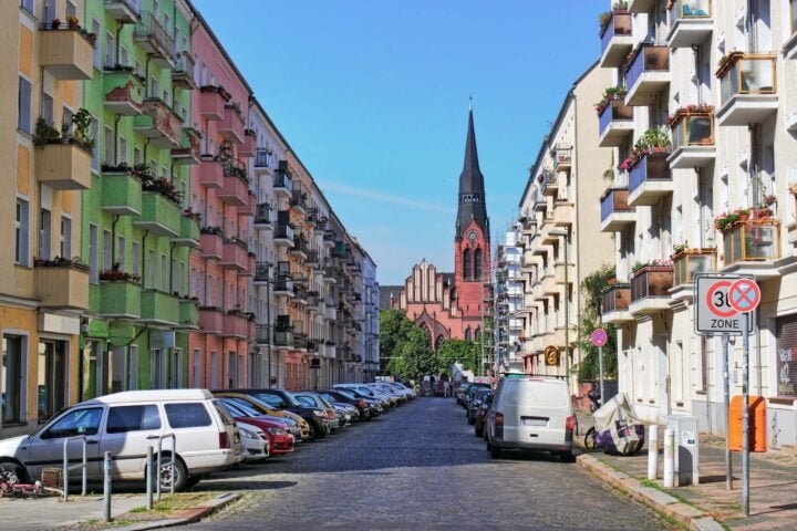 A cobblestone street in Berlin with cars parked on the left and right