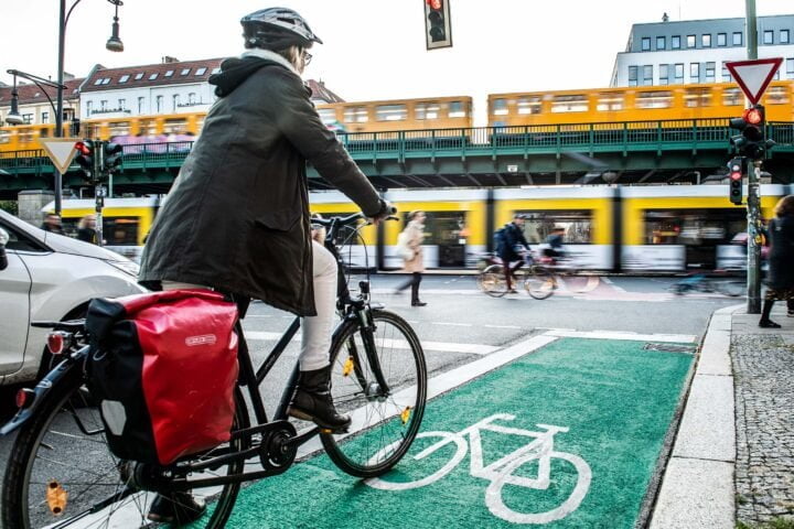 Im Vordergrund eine Fahrradfahrerin auf einem neuen grünen Radweg, im Hintergrund U und Tram